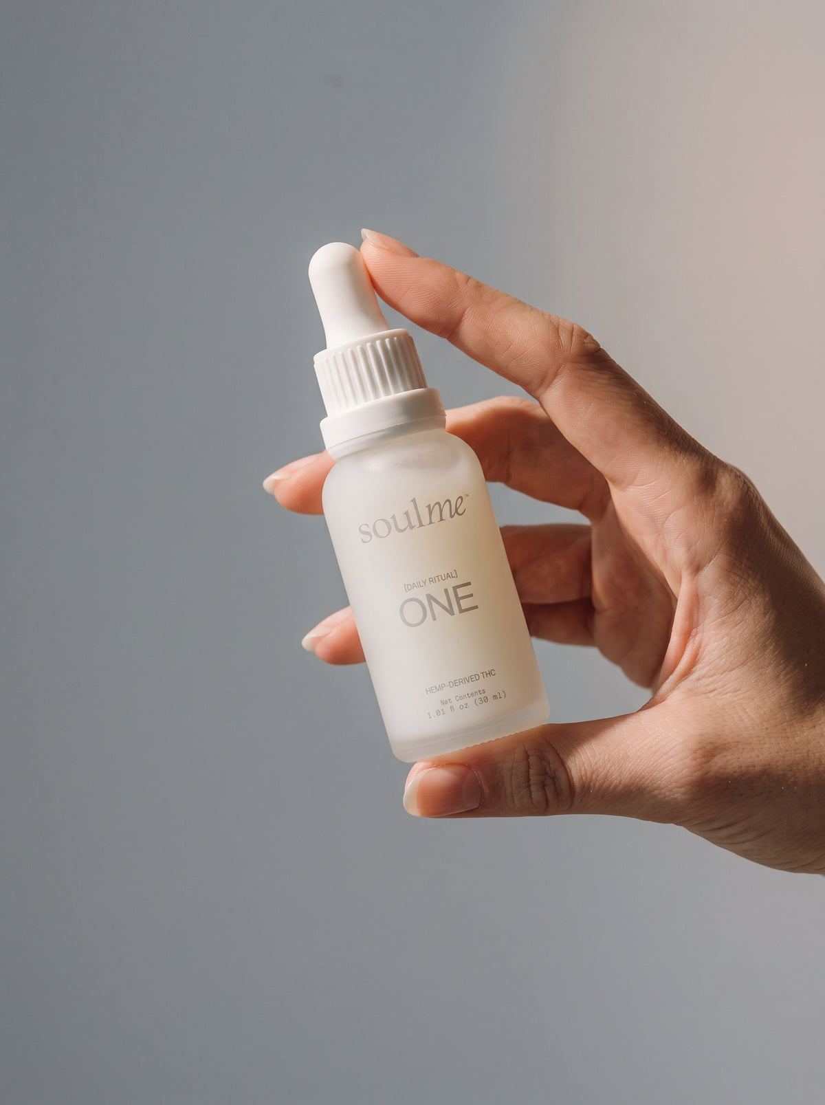 Hand holding a SoulMe ONE frosted glass dropper bottle