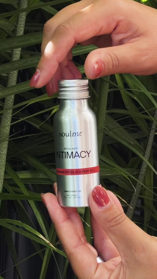 Hands opening a SoulMe Intimacy Ritual Shot among green leaves